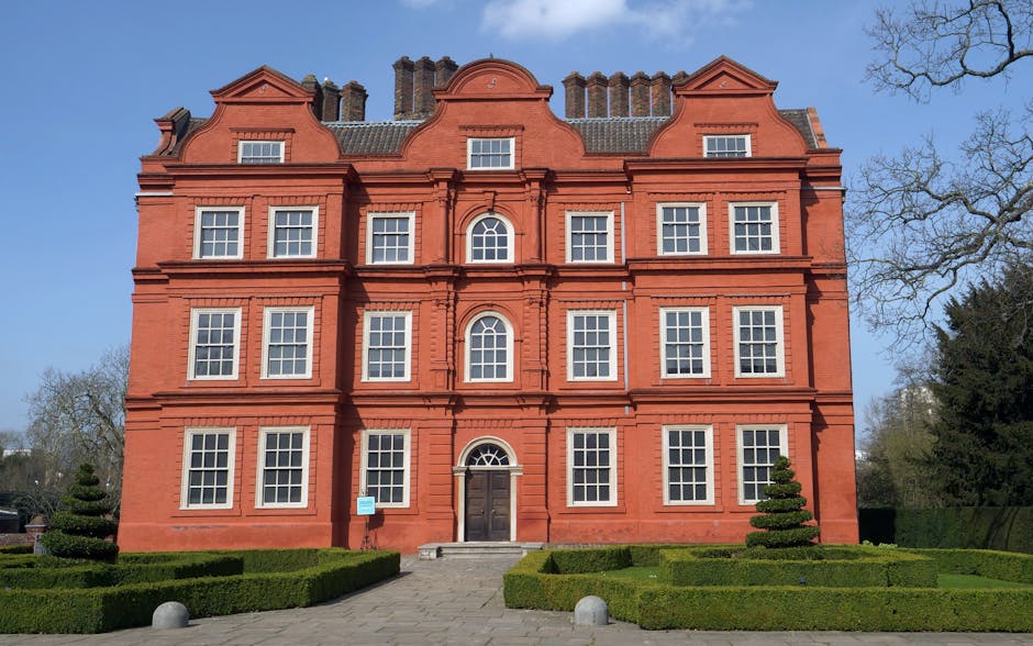A tall, multi-story Victorian-style residential building made of grey brick with decorative white trim, situated on a street lined with parked cars including a silver sports car, a black hatchback, an