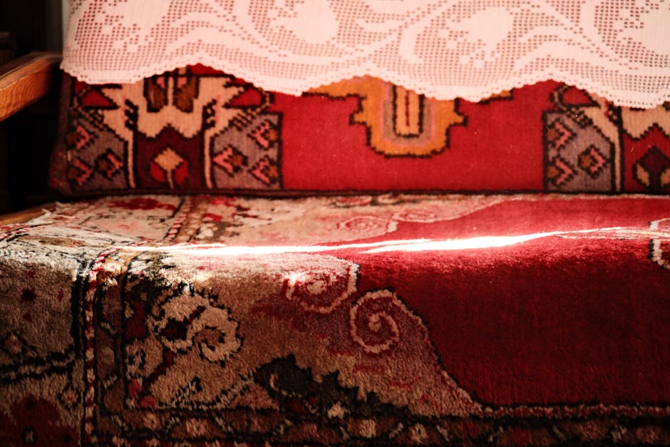A person using a handheld upholstery cleaning machine on a beige fabric car seat or sofa cushion, which has a textured area with small perforations. The cleaning device, connected to a hose, is pressed firmly against the fabric, and the surface appears damp from the cleaning process. The surrounding area of the upholstery is clean, and the scene is well-lit, highlighting the surface being cleaned. The image exemplifies professional surface cleaning and sanitisation service offered by Carpet Cleaning Finsbury Park, focusing on deep cleaning and hygiene of upholstered furniture surfaces.
